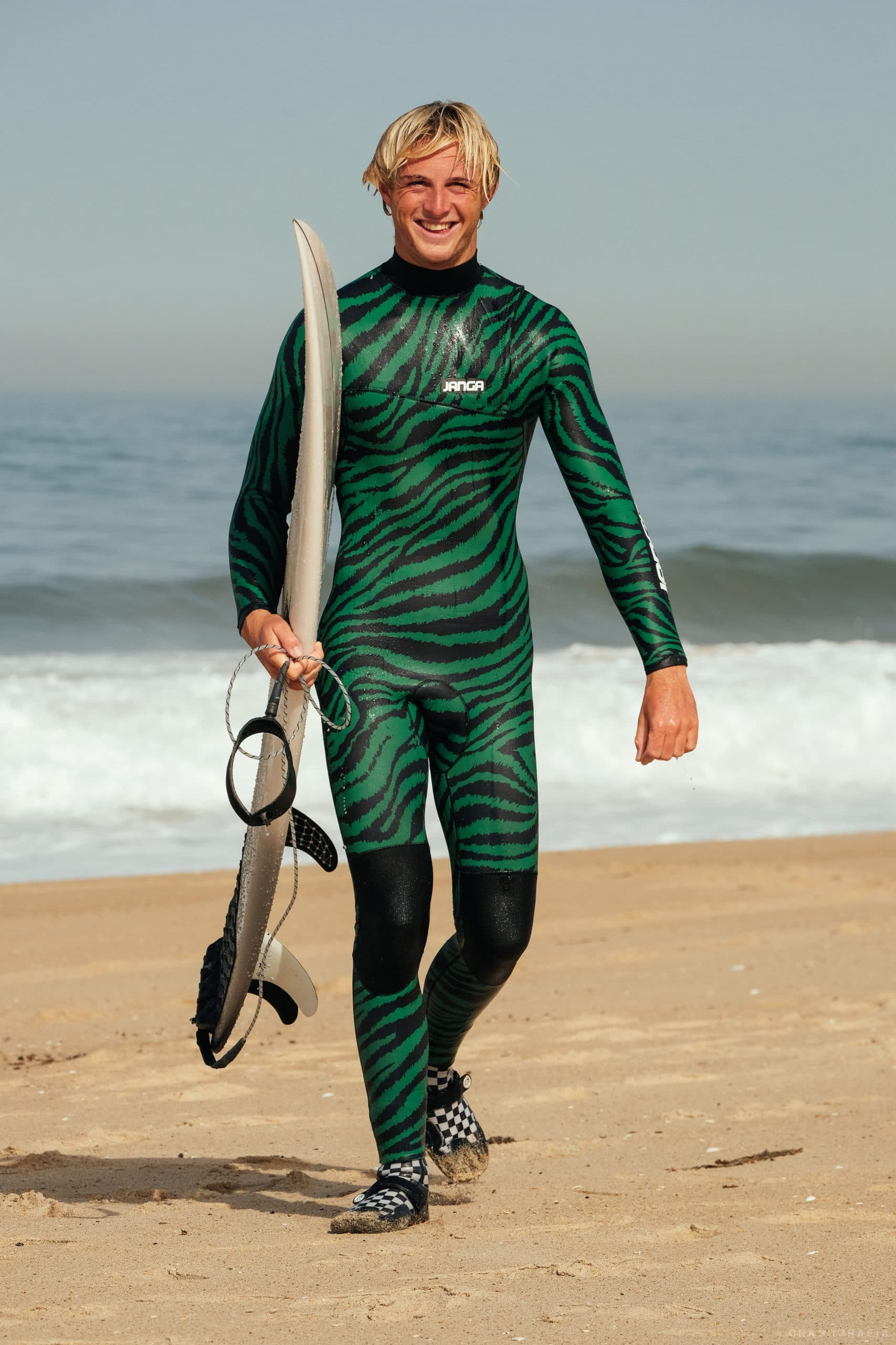 london in stripped green suit with board walking up beach